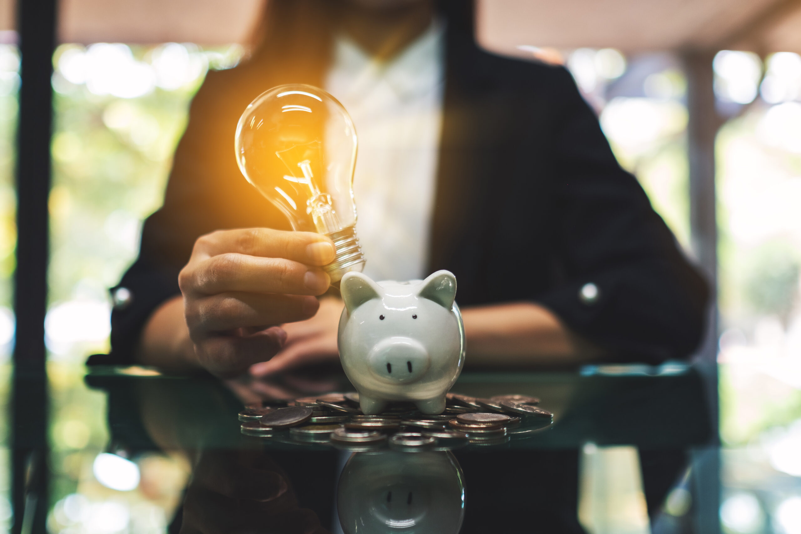Business-related Statements illustration: a businesswoman putting light bulb over a piggy bank on pile of coins on the table for saving money concept
