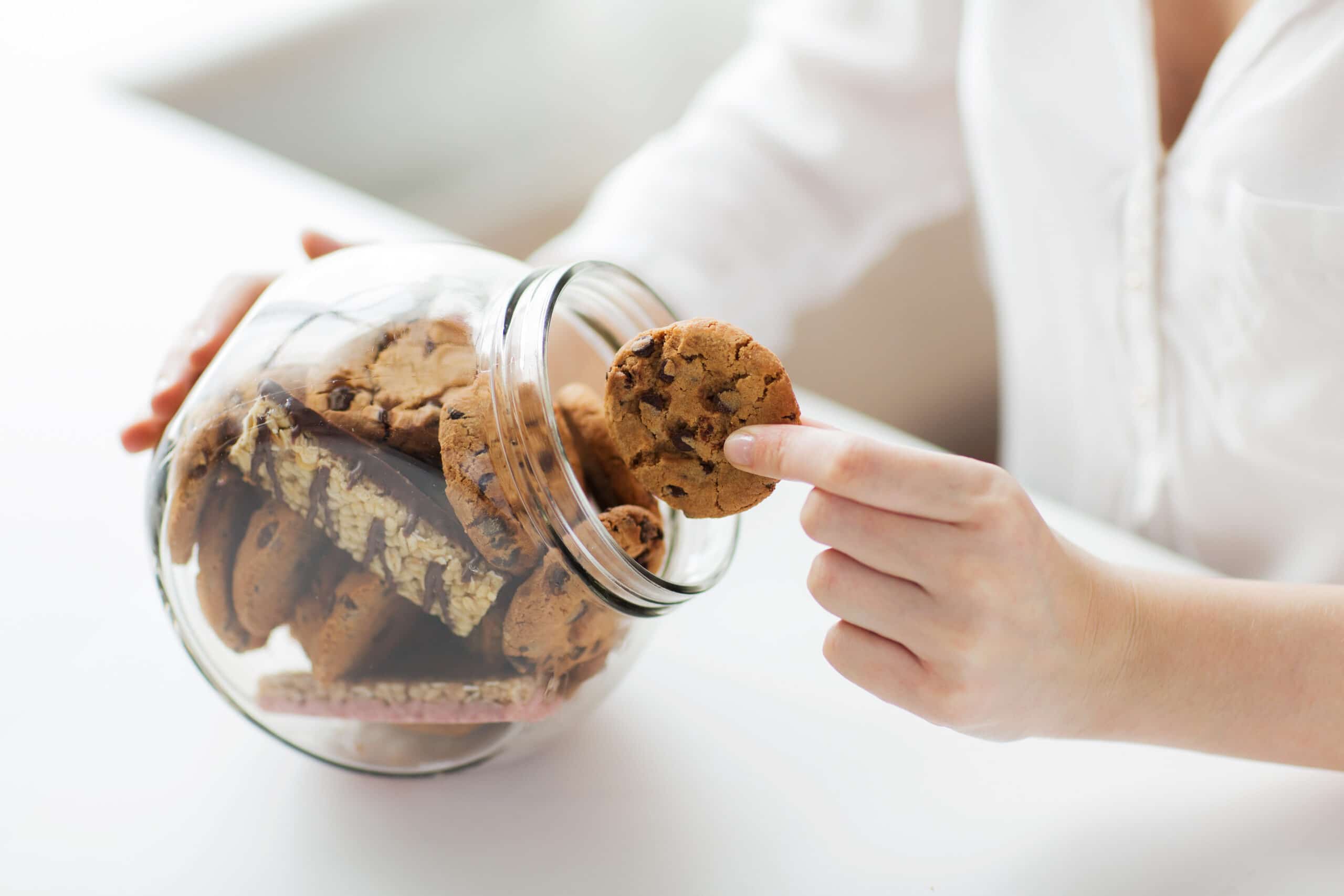 Cookies policy: people, junk food, culinary, baking and unhealthy eating concept - close up of hands with chocolate oatmeal cookies and muesli bars in glass jar