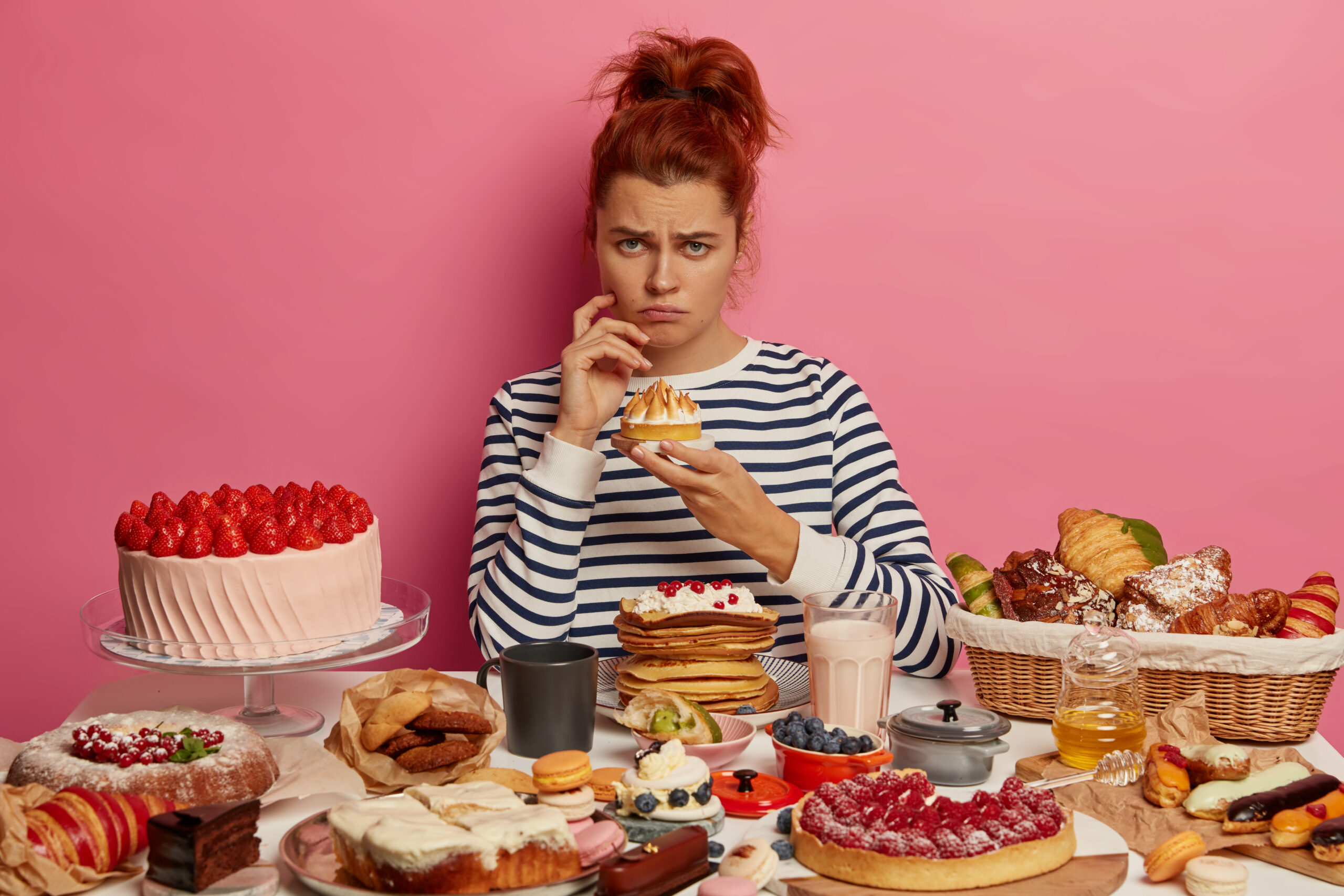 End justify means illustration: dissatisfied redhead girl in striped jumper has sweet food addiction, fed up with diets, eats various cakes, pies and other tasty desserts, has delicious lunch at home, looks sadly and gloomy