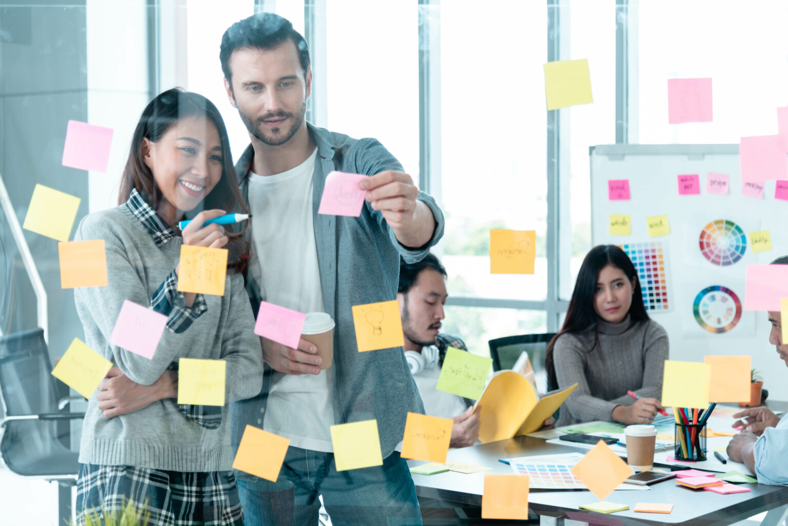 Four coworkers are illustrating a groupware system with post-its at the office