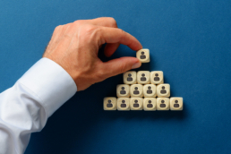 Male hand stacking wooden dices with person icons on them in a pyramids shape in a conceptual image of business hierarchy for illustrating human resources management software. Over navy blue background.