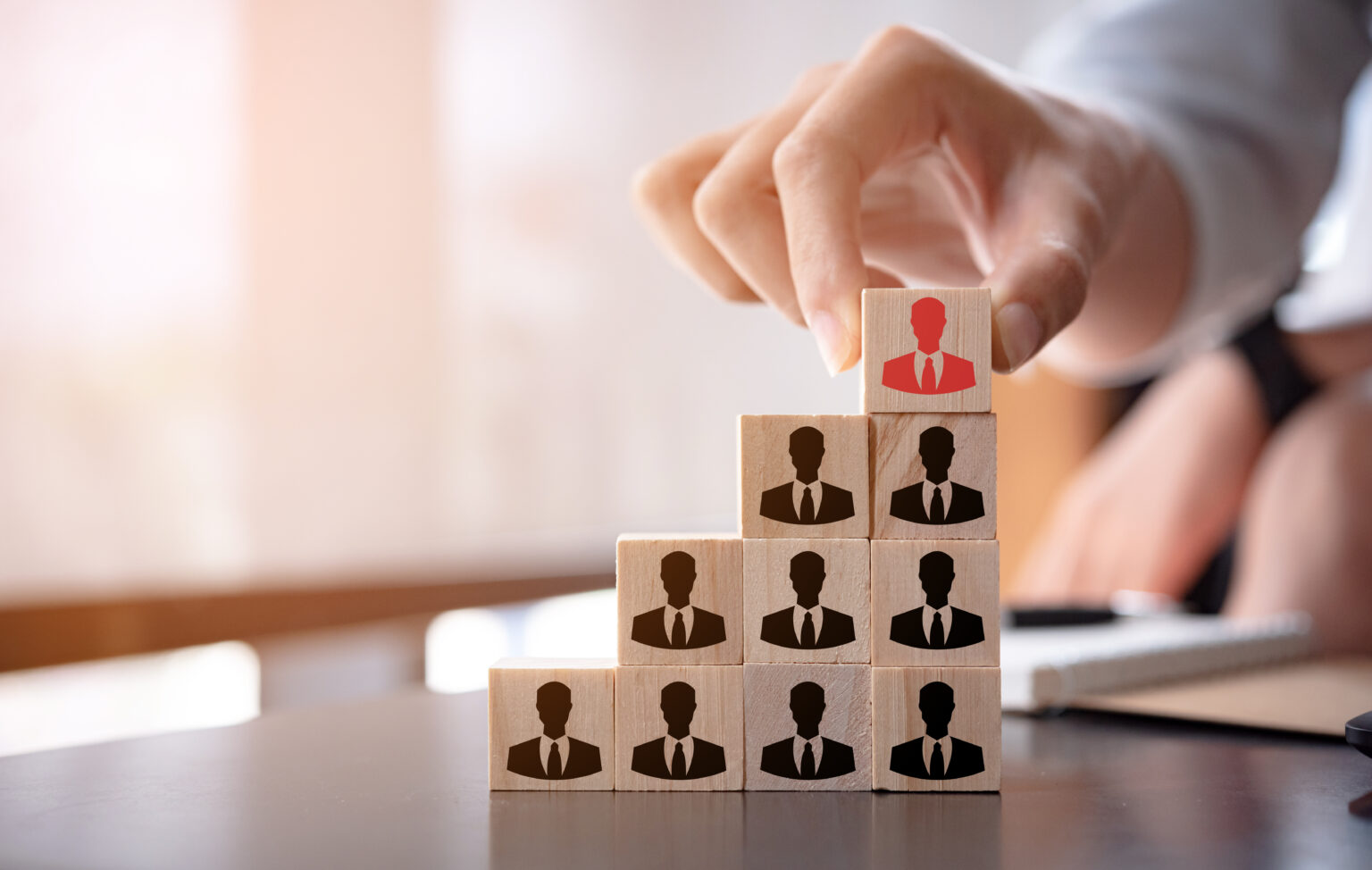 There is another man stacking wooden dices with person icons on them representing ten employees of an organisation and illustrating human resources management software.