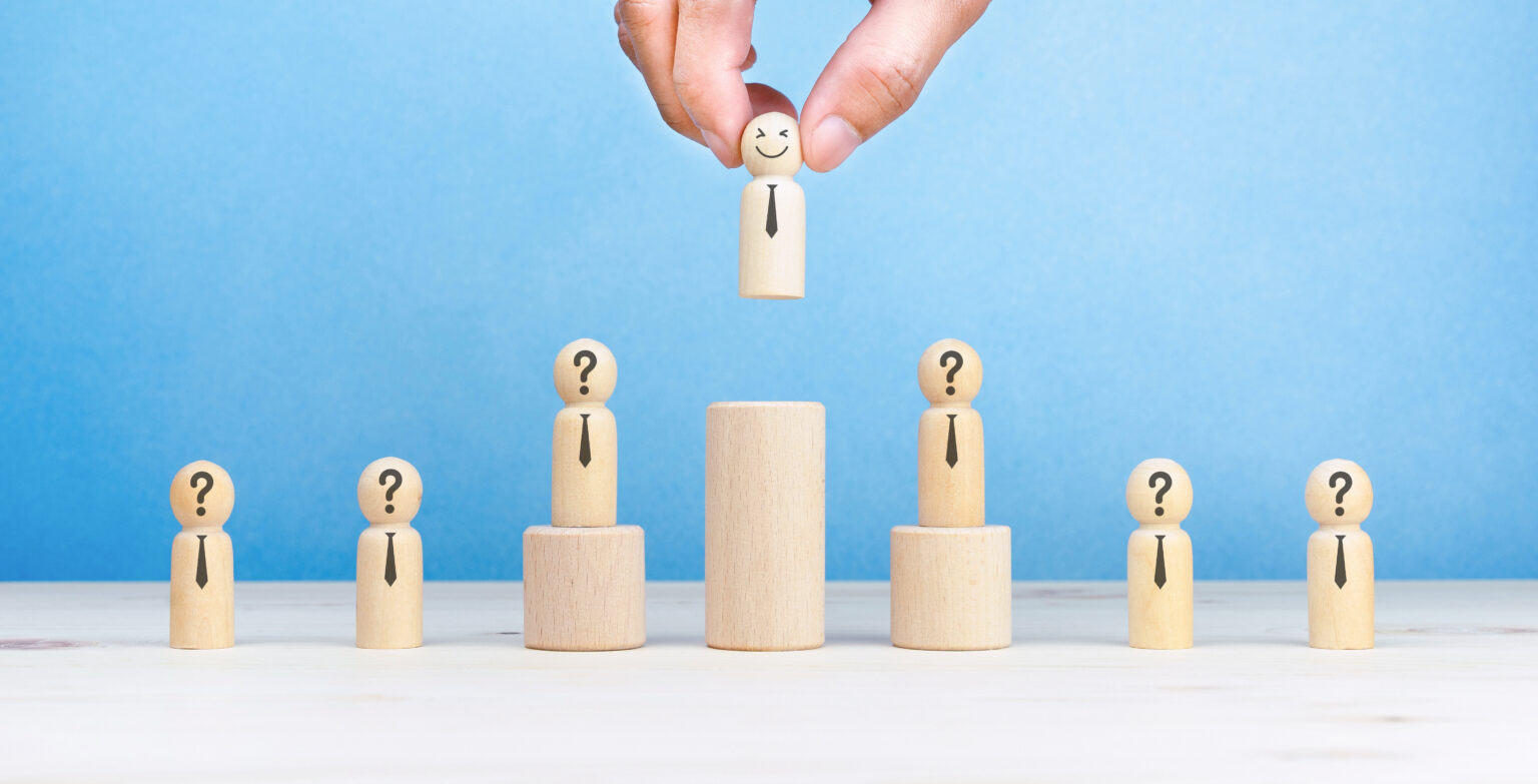 There is a man stacking wooden dices with person icons on them representing a corporate hierarchy and illustrating human resources management software.