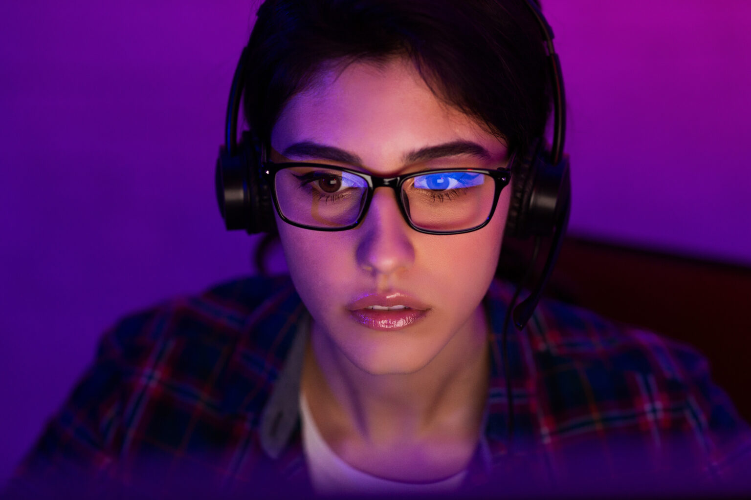 There is a female programmer working on laptop late at night. Room illuminated by neon light purple, great face illustrating Information Security topic and the CICO job title