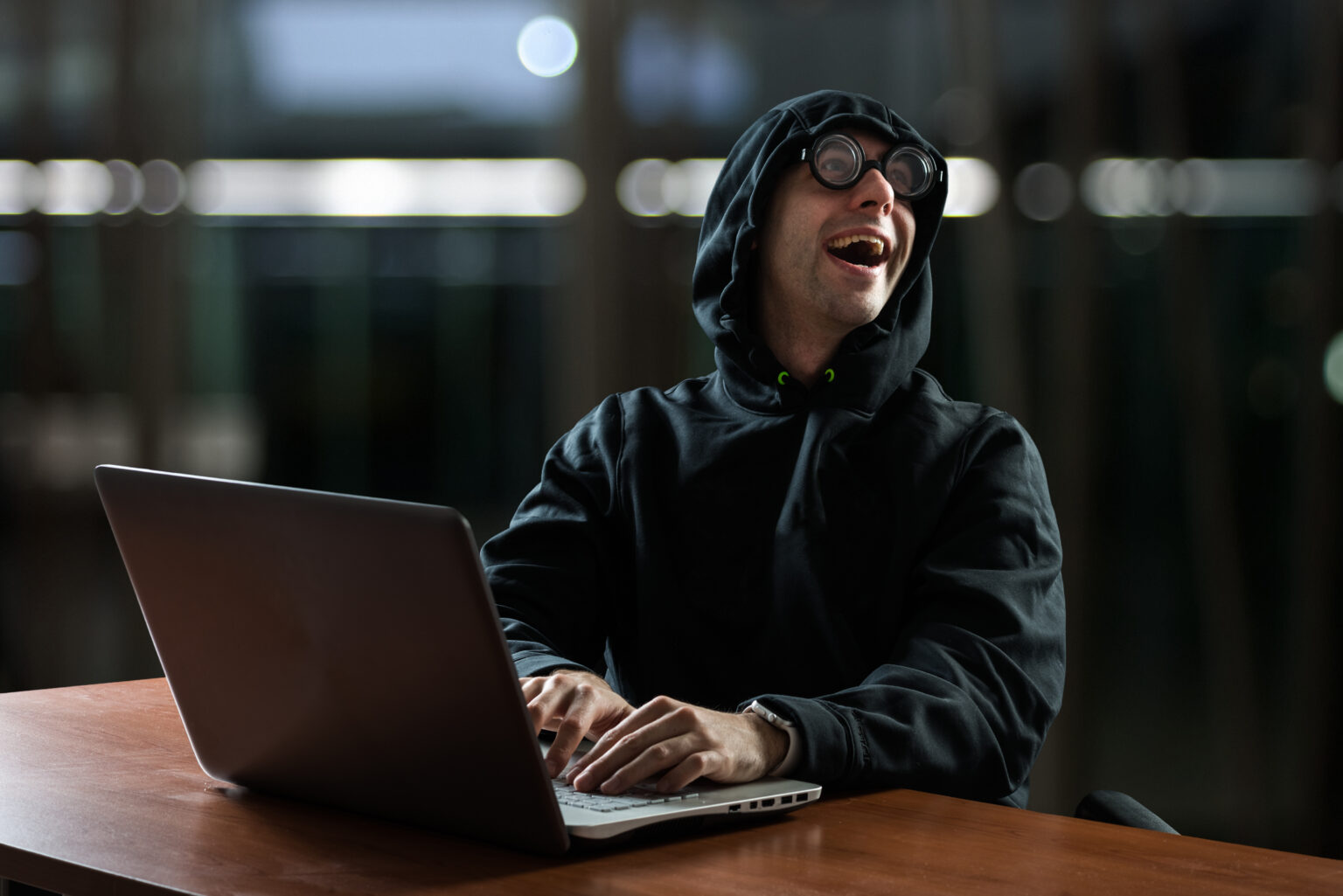 There is a male hacker in front of his computer laughing and happy of what he has done, illustrating Information Security topic