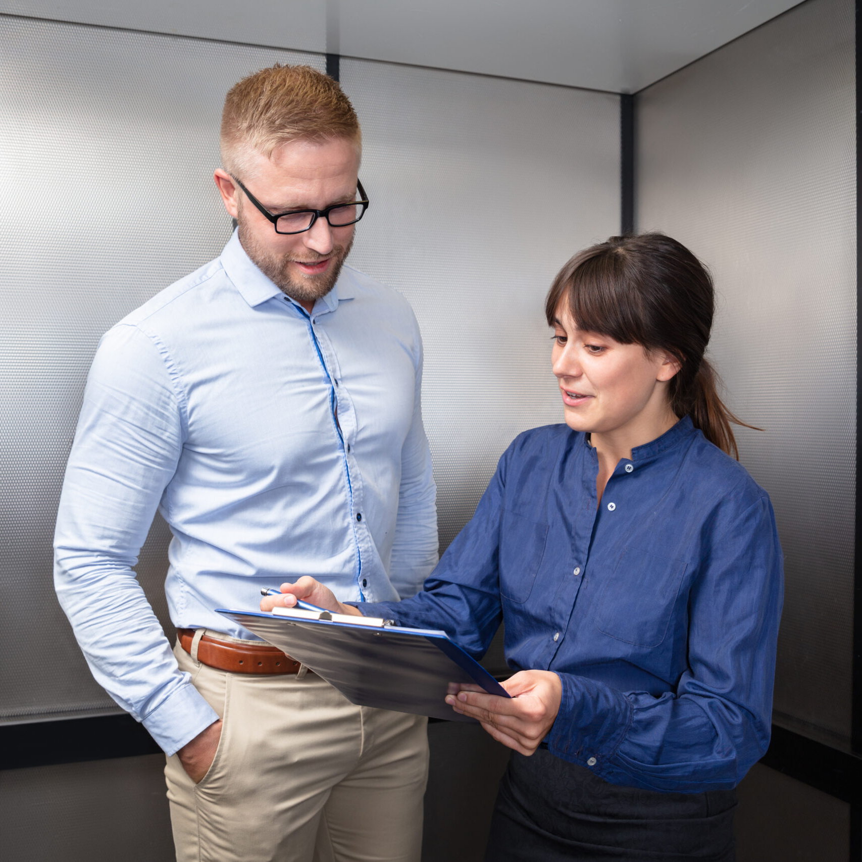 Pitch Deck: Businessman And Businesswoman Having Discussion On Business Issue Over Clipboard In Elevator