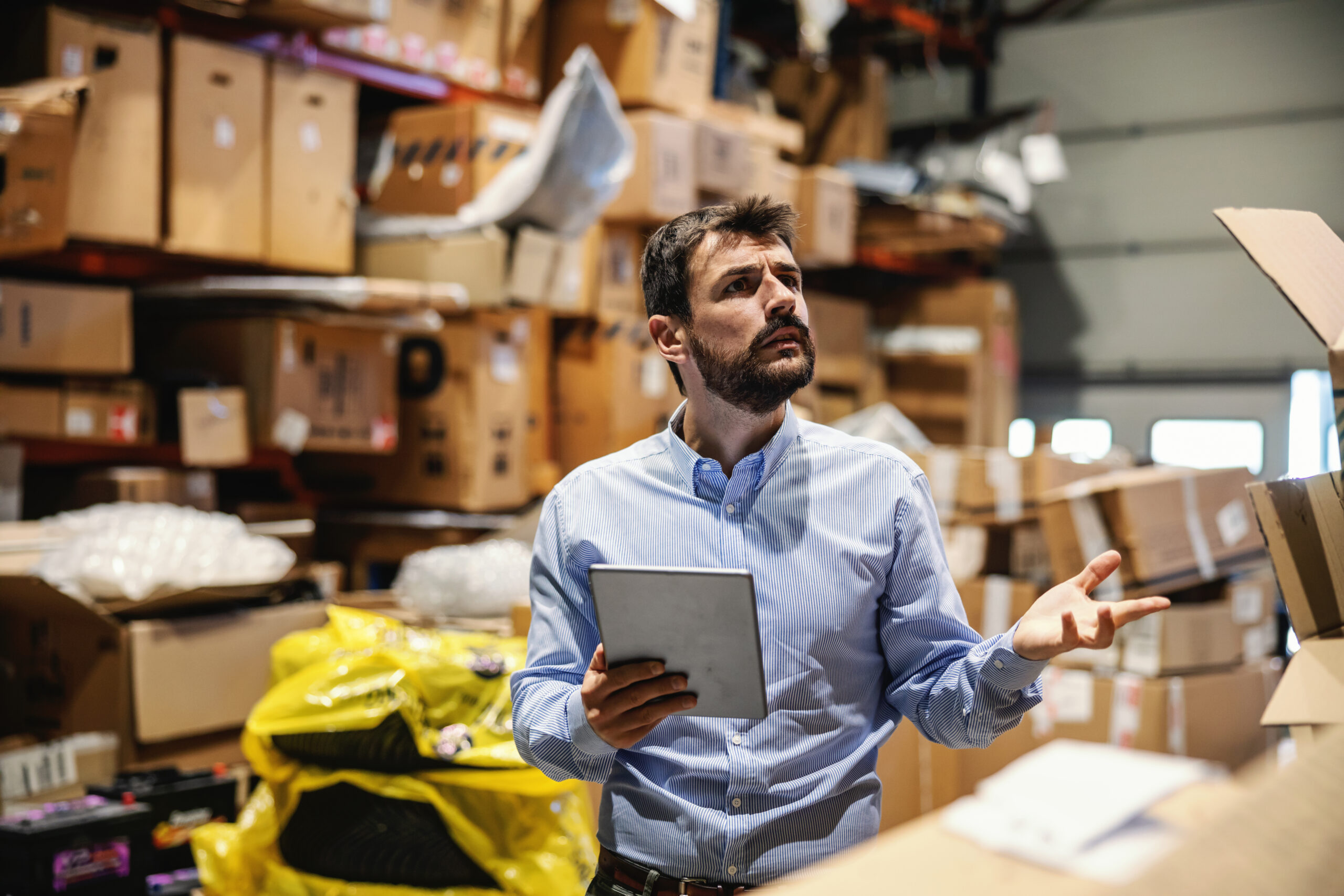 Illustration of Supply Chain Management software: confused chief standing in storage full of boxes ready for shipment and holding tablet. He is checking on goods. Export firm.
