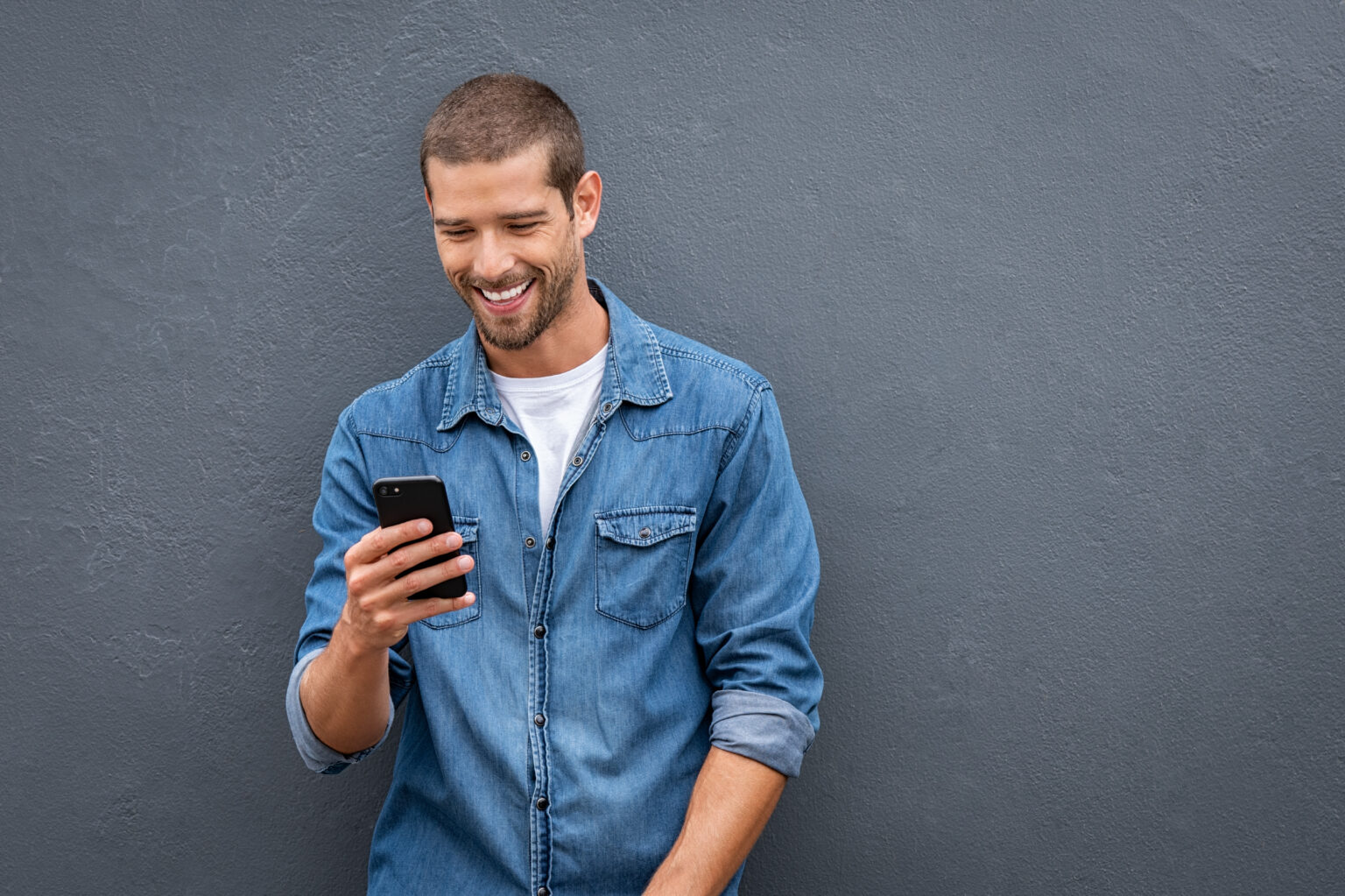 There is a cool smiling man using smartphone on grey wall, happy about the requirements of the integration